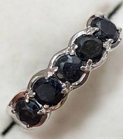 Close-up of the silver ring showing five dark blue sapphire stones set in prong settings with a wave-like silver design between stones.
