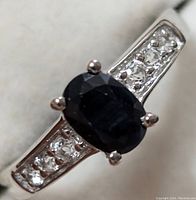 Close-up front view of silver ring with central oval blue sapphire and white topaz accents on the band.