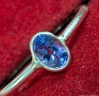 Close-up of silver ring with oval tanzanite gemstone on a red velvet background.