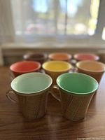 Photo of 8 vintage insulated mugs with textured raffia-style exterior pattern and colorful interiors.