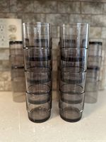 Stacked arrangement of multiple tall vintage smoky translucent black glass tumblers in Mid-Century Modern design style.