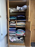 Full view of wooden closet shelves filled with multiple stacks of folded fabrics in various colors.