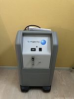 Front view of a gray Longevity Resources oxygen concentrator showing control panel with power switch, control knob, and flow meter.