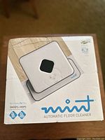 Box front showing image of Mint automatic floor cleaner with branding and features such as sweeps and mops floors.