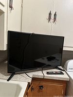 Wide shot of the Sceptre monitor on a countertop with power cable and remote control placed in front