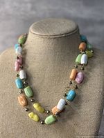 Necklace showcased on a beige fabric bust, showing chunky pastel beads in multiple colors strung together with small gold-toned spacers.