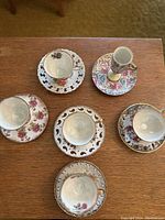 Overview of six vintage floral teacup and saucer sets arranged on wood surface showing variety of floral patterns and saucer styles