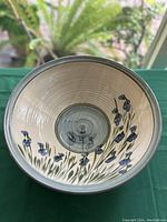 Close-up photo showing the interior of the bowl with hand-painted blue flowers and green leaves on concentric beige rings.