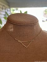 Front view of vintage gold-tone necklace with triangle-shaped rhinestone pendant on display bust.