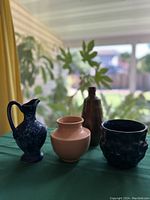 Four vintage glazed ceramic vessels on a green cloth with window background, showing the whole set.