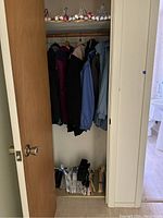 View of closet hanging six jackets of different colors and styles with folded scarves or fabric items on floor underneath.