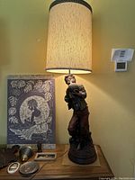 Vintage carved wooden boy holding pitcher lamp with beige cylindrical shade, standing on a base designed as a tree stump and roots, 53.5 inches tall.