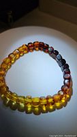 Natural light photo of the amber bracelet arranged in a circle showing gradient color transition from yellow to dark brown cube cut beads.