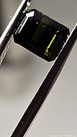 Close-up photo of an emerald cut green tourmaline gemstone held by tweezers, showing deep green color and high clarity.