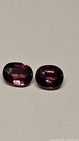 Paired untreated sapphires showing electric purple-pink-red color and good clarity on neutral background.