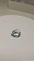 Pear cut blue aquamarine gemstone placed on a white surface showing shape and color