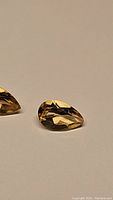 Close-up photo of two pear cut golden citrine gemstones showing the facets and reflective luster.