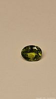 Oval cut natural apple green peridot gemstone on a neutral background, showing color and clarity.