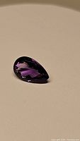 Close-up photo showing pear cut deep purple natural Brazilian amethyst gemstone on a neutral background.