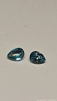 Two pear shaped lagoon blue natural zircon gemstones placed on a pale surface showing front view.