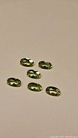 Six oval cut apple green peridot gemstones arranged on a plain background.
