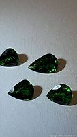 Four pear-shaped green tsavorite garnet gemstones on a neutral surface