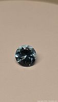 Close up photo of round diamond cut Swiss blue topaz gemstone on neutral light background showing facets and blue lagoon color