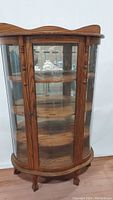 Full view of the curved solid oak curio cabinet with glass paneled door and visible wooden shelves inside.