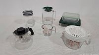 Full set of glass kitchen items including canister, Bormioli Rocco jug, glass storage container, Melitta carafe, measuring cup with juicer lid.