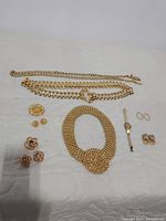 Overview of all gold-tone jewelry and accessories laid out on white quilt.
