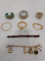 Top-down photo of all 8 bracelets arranged on white quilted surface showing variety of metals and stones.