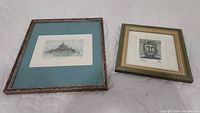 Two framed prints placed on a white surface: the left artwork is a watercolor lithograph of Le Mont Saint Michel, the right artwork is a lithograph print depicting a stylized head, both signed and dated 1990.