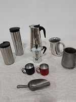 Full set of items including tumblers, espresso makers, mugs, and scoop arranged on white fabric