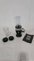 Overview of Ninja Fit Blender components including base, blending cups, lids, and manual spread out on white cloth background