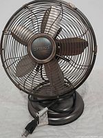 Front view of the Optimus copper tint electric fan showing the blades, grill, base, and attached power cord.