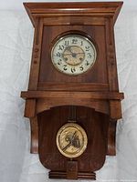 Full view of the wooden wall pendulum clock showing the carved case, clock face, and pendulum.