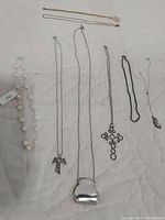 Eight necklaces and chains laid out on a white cloth. Varied styles including pearls, metallic pendants, and plain chains. Shows overall lot content.