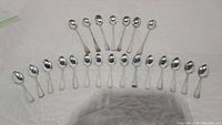 24 silver-plated teaspoons arranged in two rows on a cloth