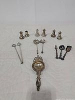 Group photo of 3 sets of salt and pepper shakers, along with utensils and tea strainer on white surface.