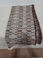 Full view of folded woven blanket showing the brown, blue, burgundy, and white woven pattern and fringed edge
