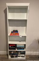 White wooden bookshelf filled partly with various books, some shelves partially empty