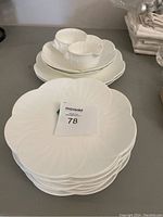 Six white porcelain flower-shaped plates and matching bowls stacked, displayed on table.