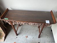 Front view of brown console table with carved wooden apron and flat wooden top.