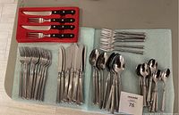 Full display of cutlery laid out on towels including forks, knives, spoons, and specialty steak knives and forks.