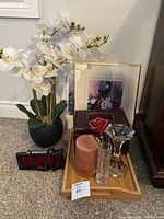 Wooden tray with candle, glass vases with fragile red rose, two floral pictures, dark brown locked jewelry box with key, artificial white orchid plant in black pot