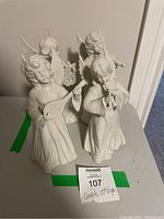 Four white porcelain angel figurines with wings, each holding musical instruments: violin, lute, flute, and French horn.