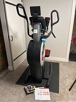 Front view of elliptical on protective mat with gloves, DVDs and paperwork at base