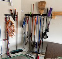 Wide view of all hanging gardening and garage tools including brooms, shovels, rakes, extension cords, and bungee cords on hooks and leaning