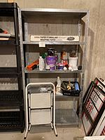 Metal shelving unit with various painting supplies including paint cans, caulking tube, tools, and U-Haul wrapping paper on top shelf.