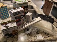 Photo showing boxed Nutri Chopper, FoodSaver vacuum sealer, vacuum bags, replacement gaskets, and Cuisinart burger press box on kitchen counter.